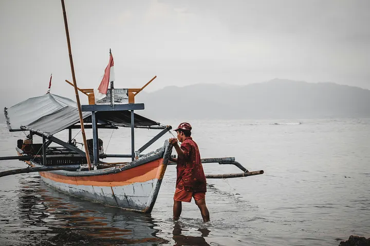 Nelayan menarik perahu tradisional di tepi laut
